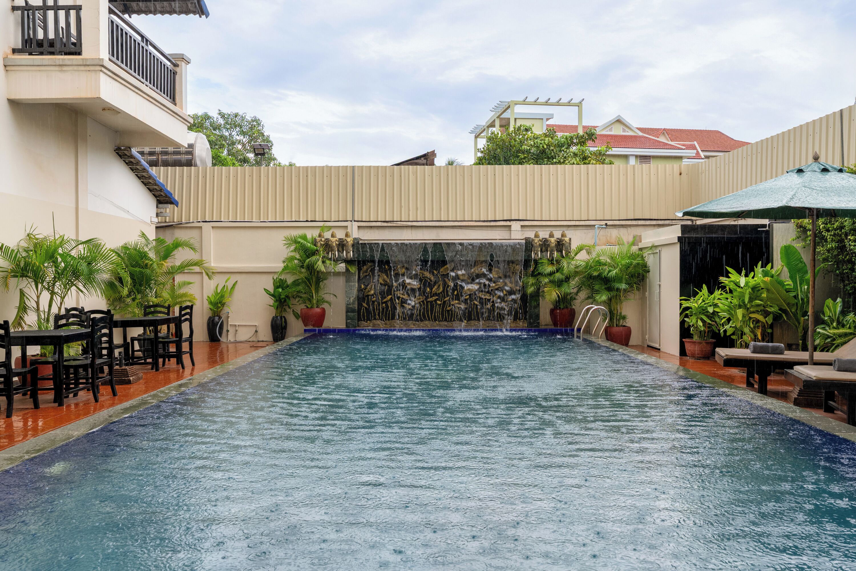 Una piscina con cascada, rodeada de plantas en macetas y muebles de exterior.