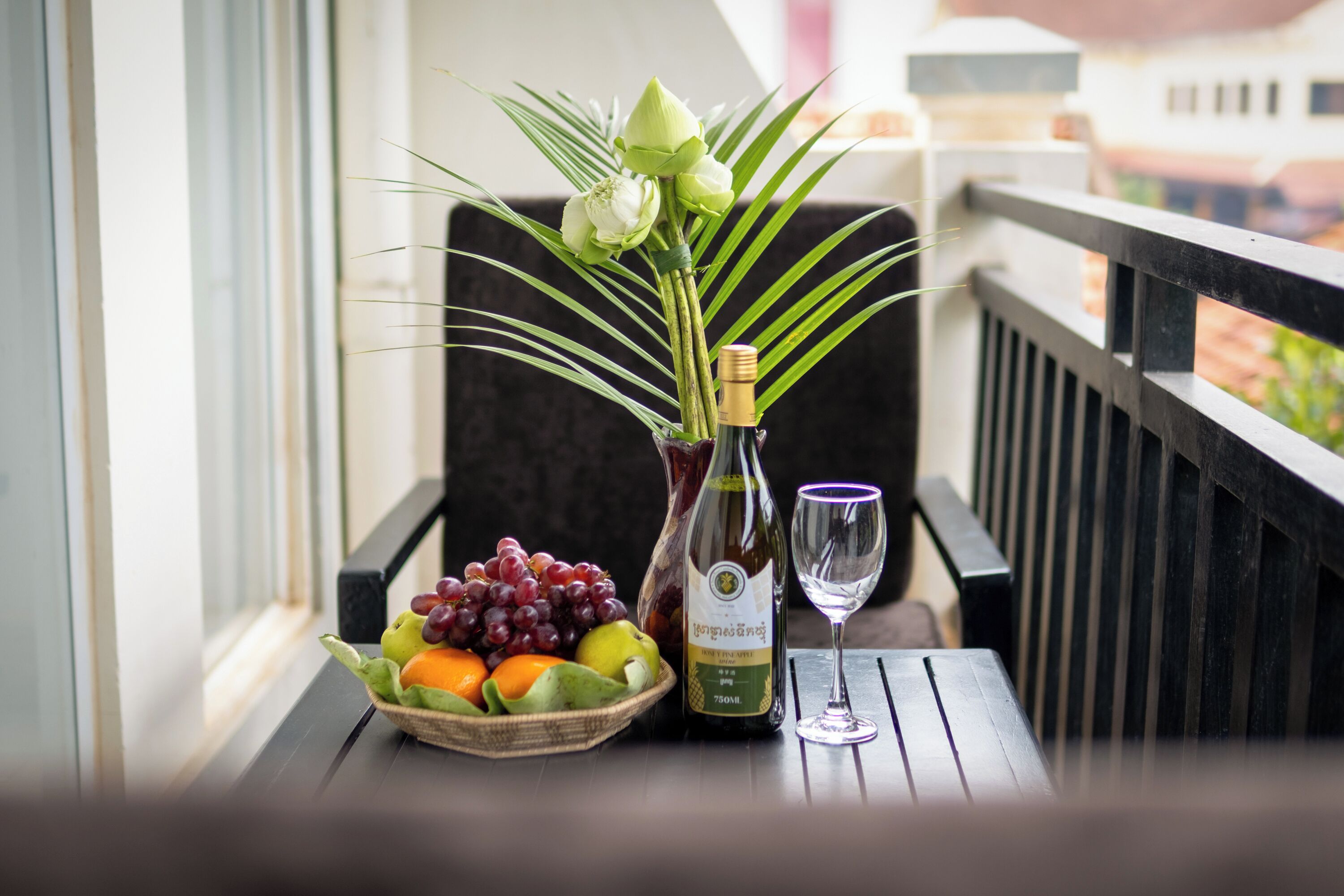 Ein Tisch mit einer Fruchtschale, einer Weinflasche und einem Glas auf einem Balkon.