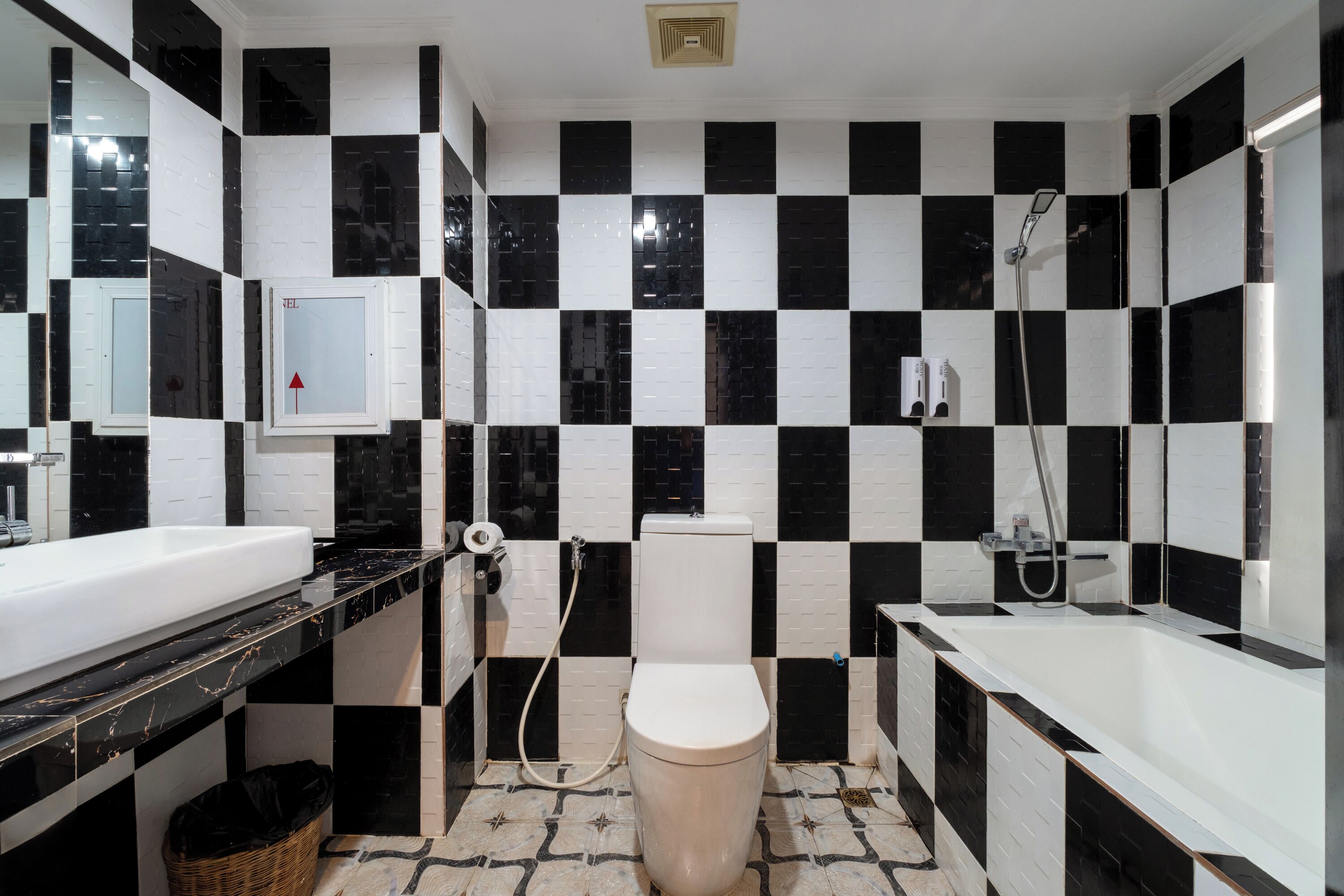 A bathroom with a black and white checkered tile wall, a white toilet, a sink with a black countertop, and a shower area.