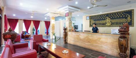 A hotel lobby with red seating, a reception desk, and a large decorative wall.