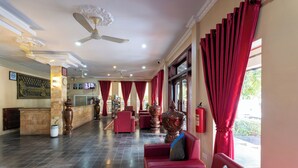 Un vestíbulo de hotel con sofás rojos, un mostrador de recepción, un jarrón grande y un ventilador de techo.