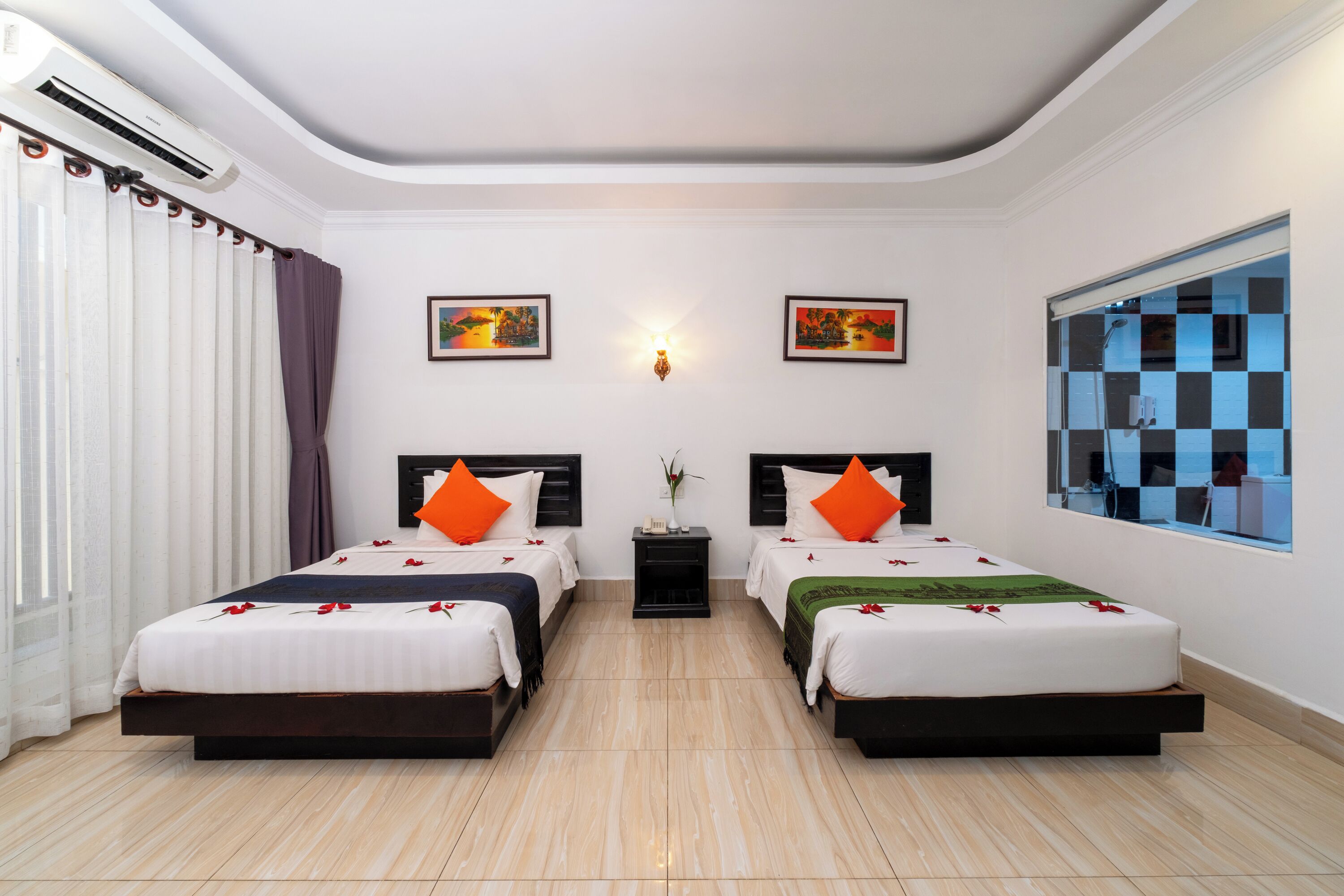 A hotel room with two beds, a large window with checkered blinds, a wall-mounted air conditioner, and two wall-mounted light fixtures.