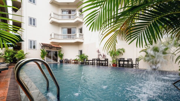 Una piscina interior con una fuente, rodeada de plantas en macetas y un edificio de varios pisos con balcones.