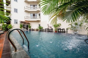 An indoor swimming pool with a water fountain, surrounded by potted plants and a multi-story building with balconies. - Khmer Angkor Residence (Siem Reap)