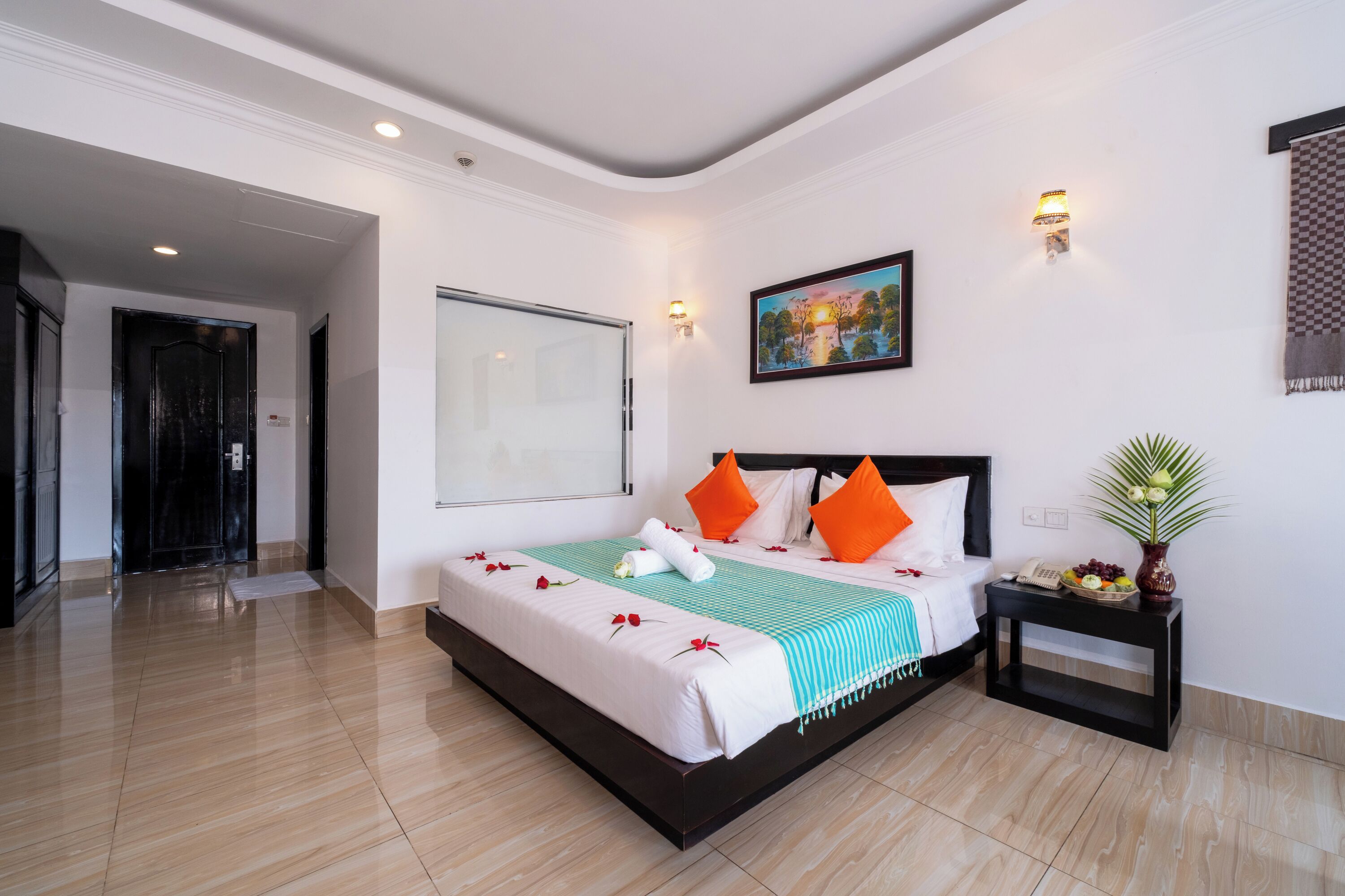 Une chambre d’hôtel moderne avec un grand lit, une table de chevet, un tableau et une porte donnant sur une autre pièce.
