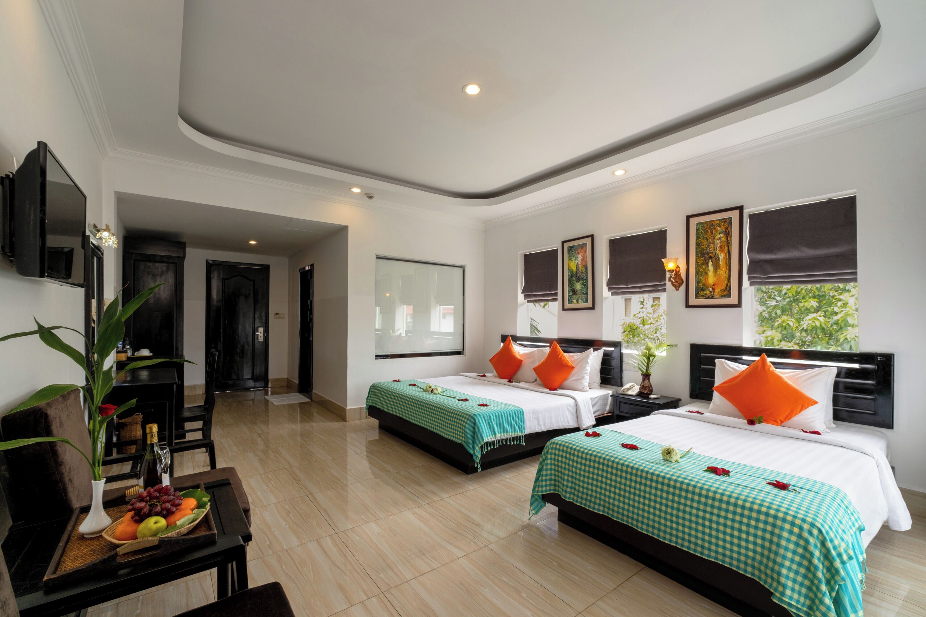 A hotel room with two beds, a dining area with a table and chairs, a TV mounted on the wall, and artwork on the walls.