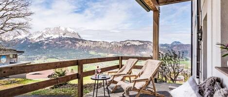 A wooden deck with two lounge chairs and a small table, overlooking a mountainous landscape.