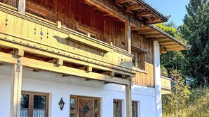 A two-story wooden building with a balcony, a wooden door, and a stone wall. - Penzing by Interhome (Sankt Johann in Tirol)