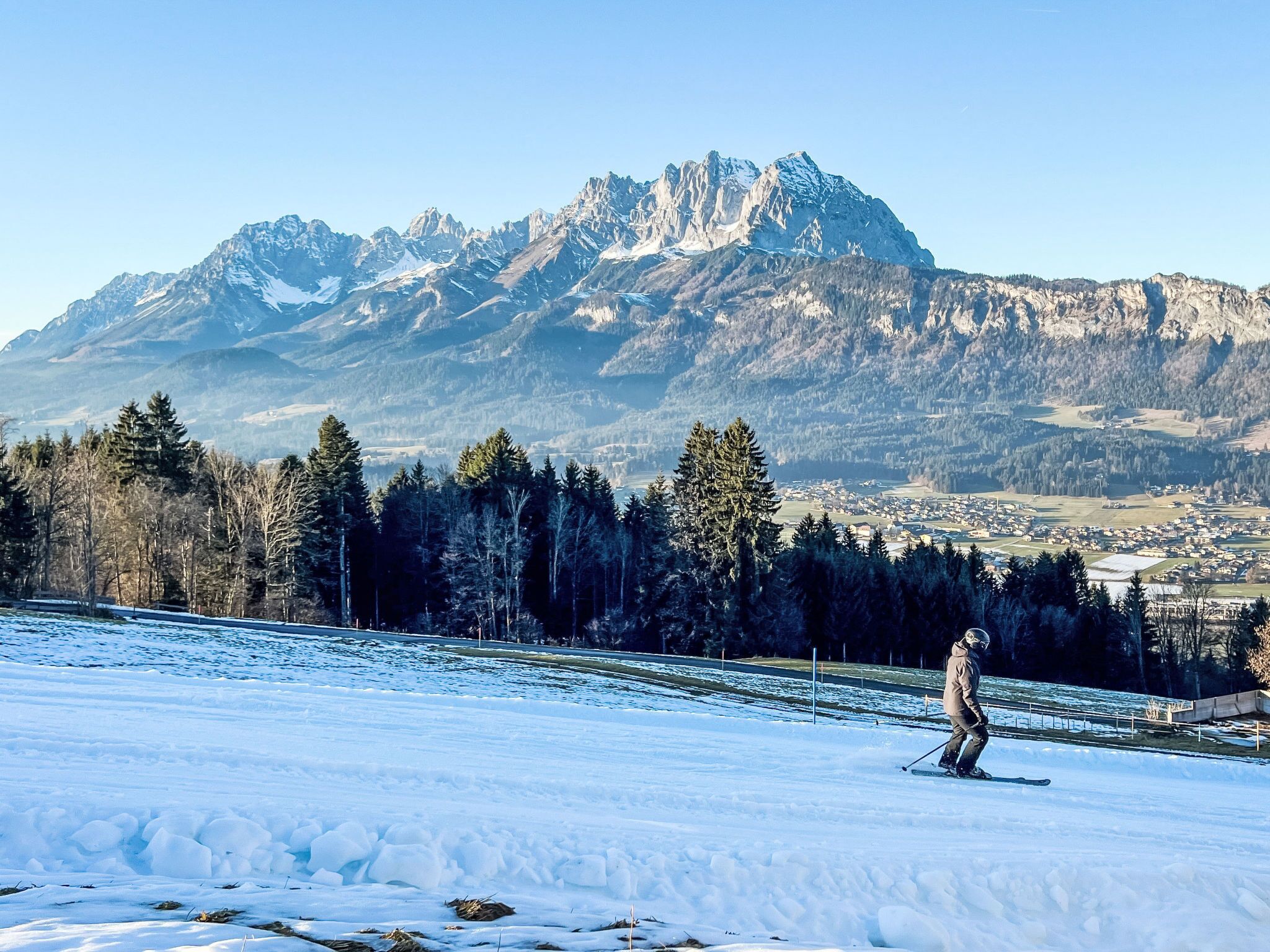 A snowy landscape with a skier, a mountain range, and a town in the background.