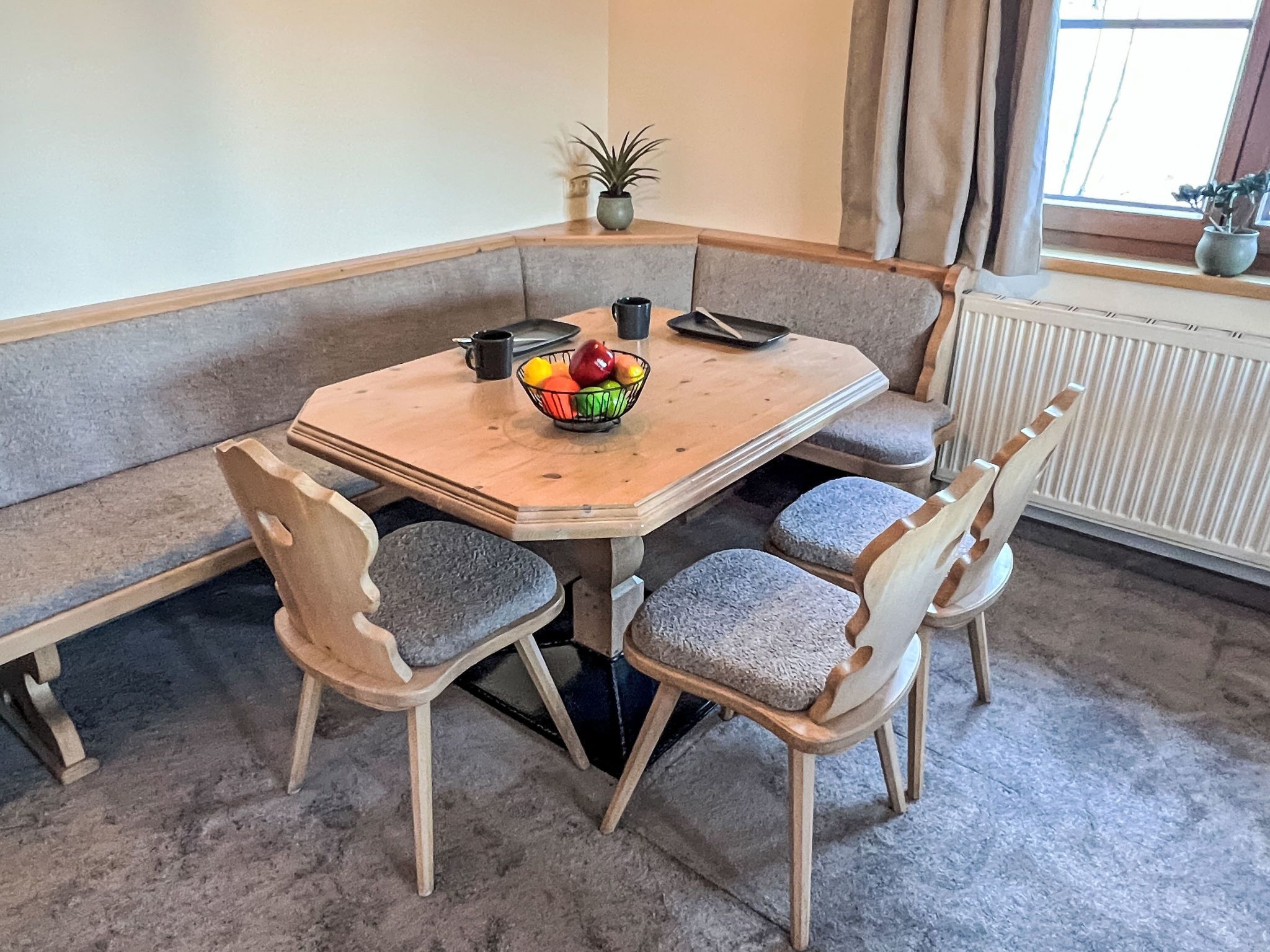 Een hoekje met een eetgedeelte, met een houten tafel, comfortabele stoelen, een schaal fruit en een potplant.