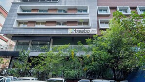 Un immeuble à plusieurs étages, avec une enseigne « Treebo » au rez-de-chaussée, des balcons et un espace de stationnement à l’avant.