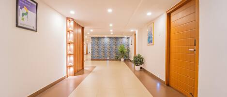 A hotel corridor with wooden doors, a patterned wall, and potted plants.
