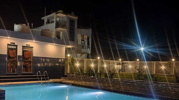 A swimming pool with a tiled deck, a modern building with multiple levels and balconies, and string lights along the fence. - Hotel The Crystal (M āvli)
