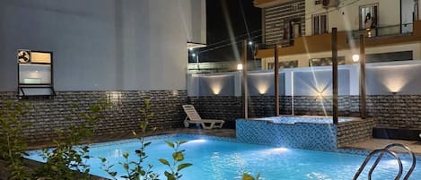 Una piscina con borde de baldosas, rodeada por un muro de piedra bajo y algo de vegetación.