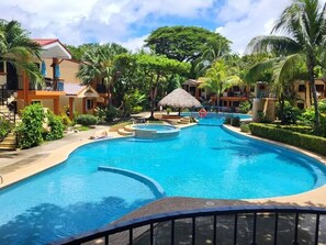 Ein Resort mit einem großen Schwimmbecken, umgeben von Palmen und Hotelgebäuden.