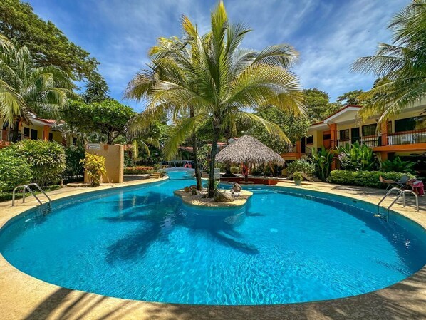 Ein kreisförmiger Pool mit einer Palme in der Mitte, umgeben von üppiger Vegetation und einer strohgedeckten Struktur.