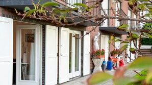 Une rangée de portes à cadre blanc, une façade en briques, des plantes en pot et une statue au rez-de-chaussée.