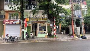 Ein Café mit Außenbestuhlung, ein Motorrad davor geparkt und ein Baum im Vordergrund.
