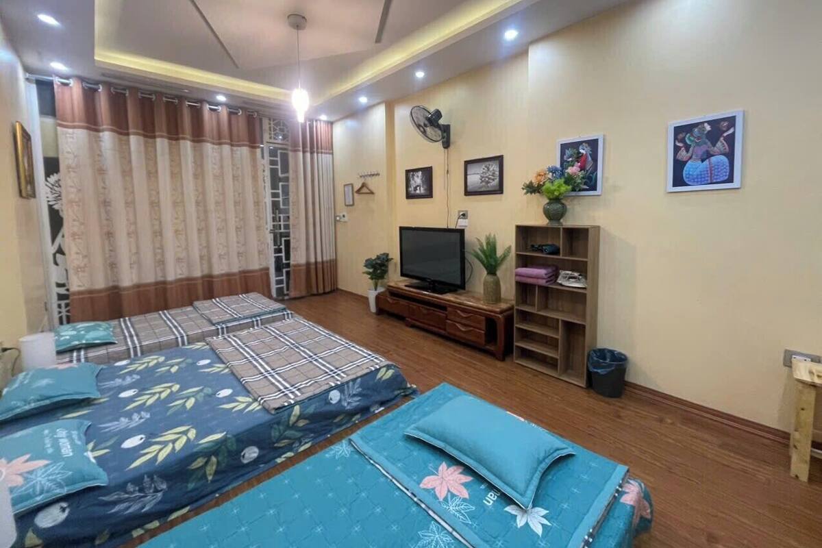 Quarto de hotel com duas camas, televisão, prateleira com objetos decorativos e um ventilador na parede.