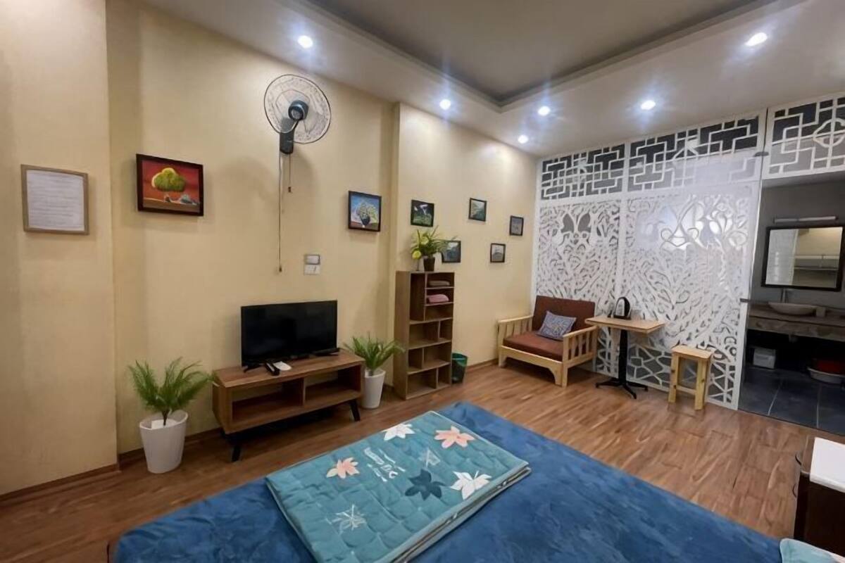 Uma sala de estar com televisão, estantes, um ventilador, um sofá e um painel decorativo.
