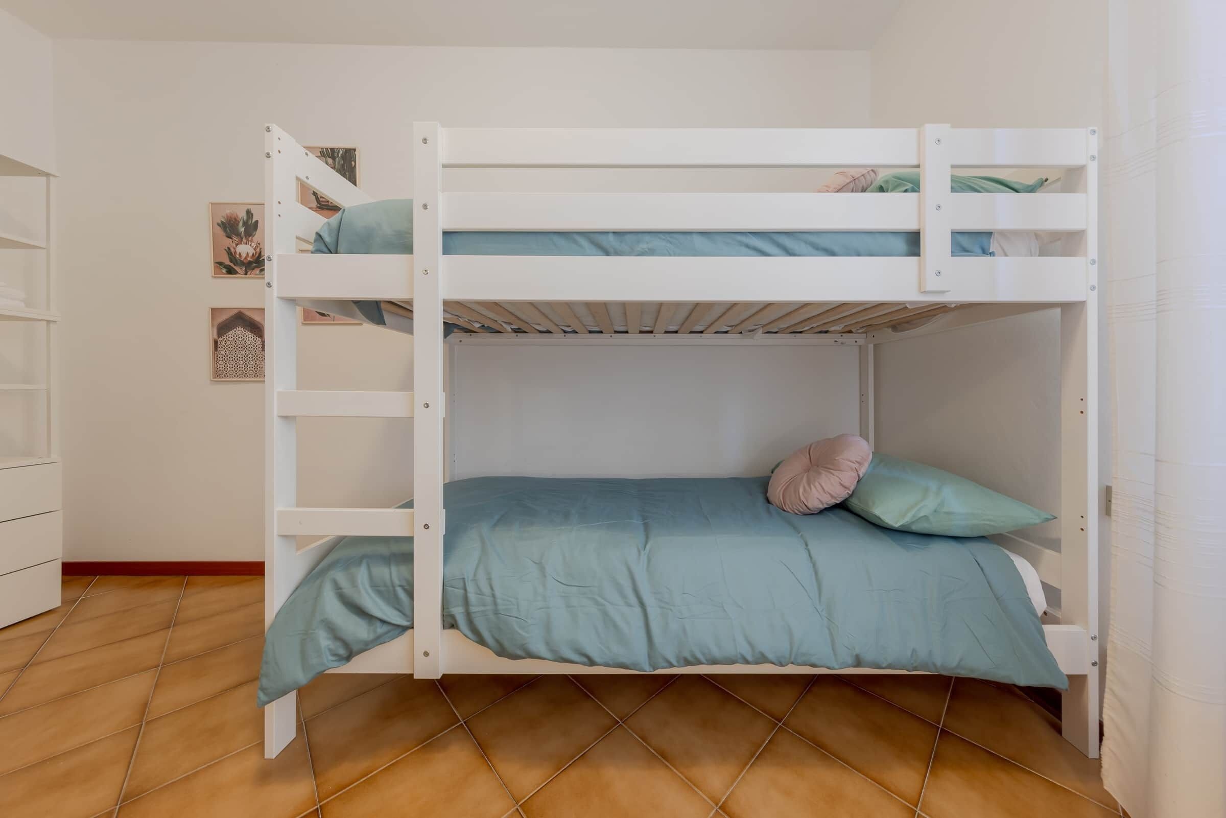Ein Stockbett mit blauer Matratze und Kissen, ein weißer Kleiderschrank und ein Fliesenboden.