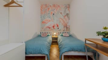 Una stanza accogliente e piccola con due letti, un tavolo di legno e un murale con fenicotteri e vegetazione.