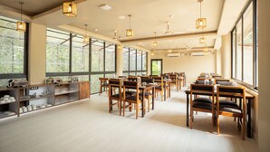 Un amplio comedor con sillas y mesas de madera, ventanas grandes y lámparas colgantes.