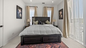 A modern bedroom with a large bed, two bedside tables, and a view of the outdoors through sheer curtains. - Festive Villa in Richardson/Dallas (Richardson)