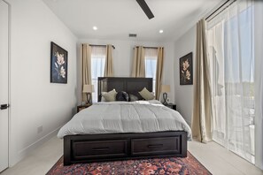 Une chambre moderne avec un grand lit, deux tables de chevet et une vue sur l’extérieur à travers des rideaux légers.