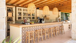 A bar area with wooden stools, a bar counter, and hanging wicker light fixtures. - Petrino Eco Village (Kassandra)