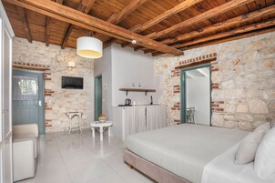 Un dormitorio con pared de piedra, vigas de madera en el techo, una cama, una mesita y un televisor.