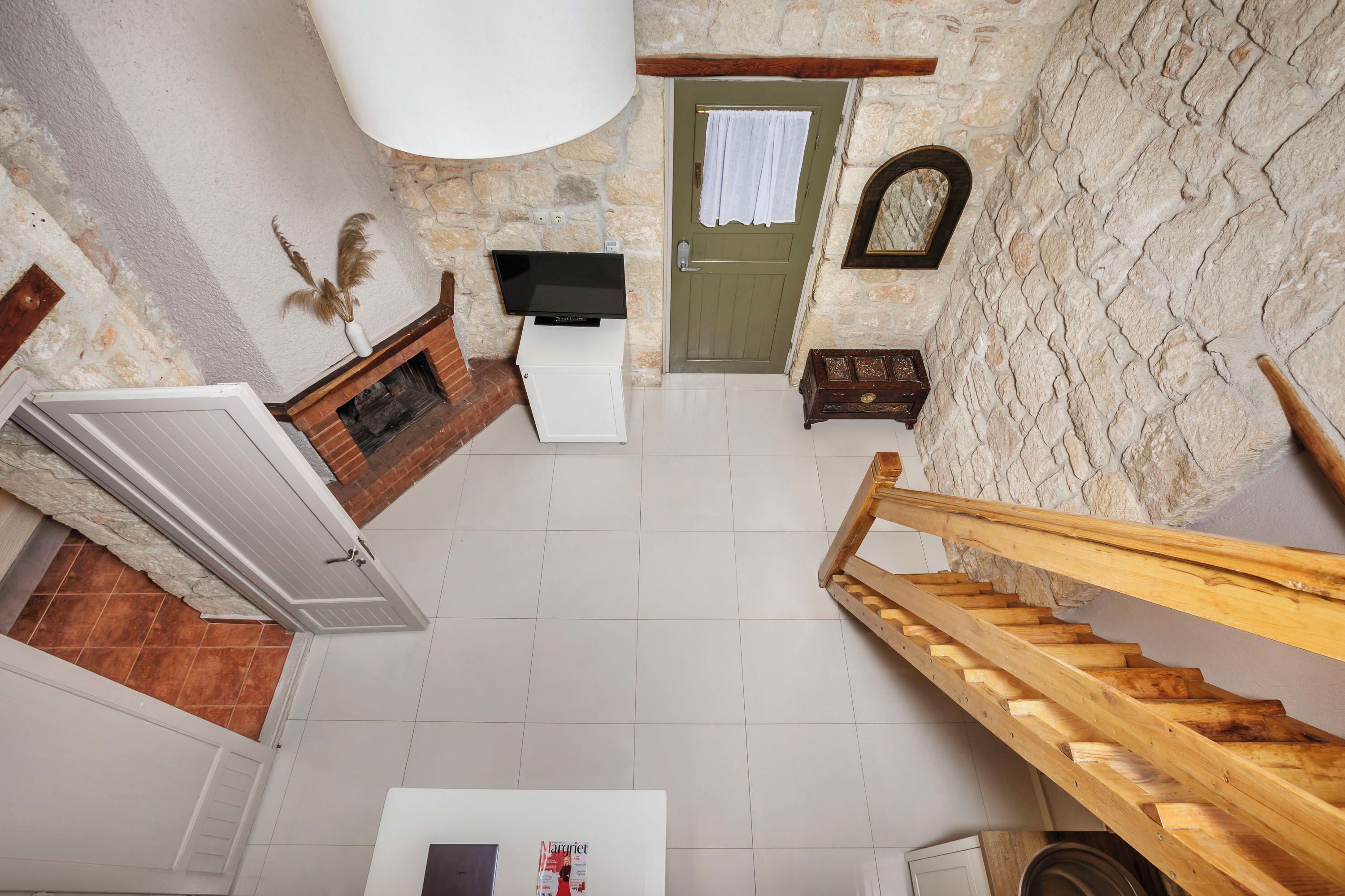 A high-ceilinged room with a stone wall, a wooden staircase, and a flat-screen TV on a white cabinet.