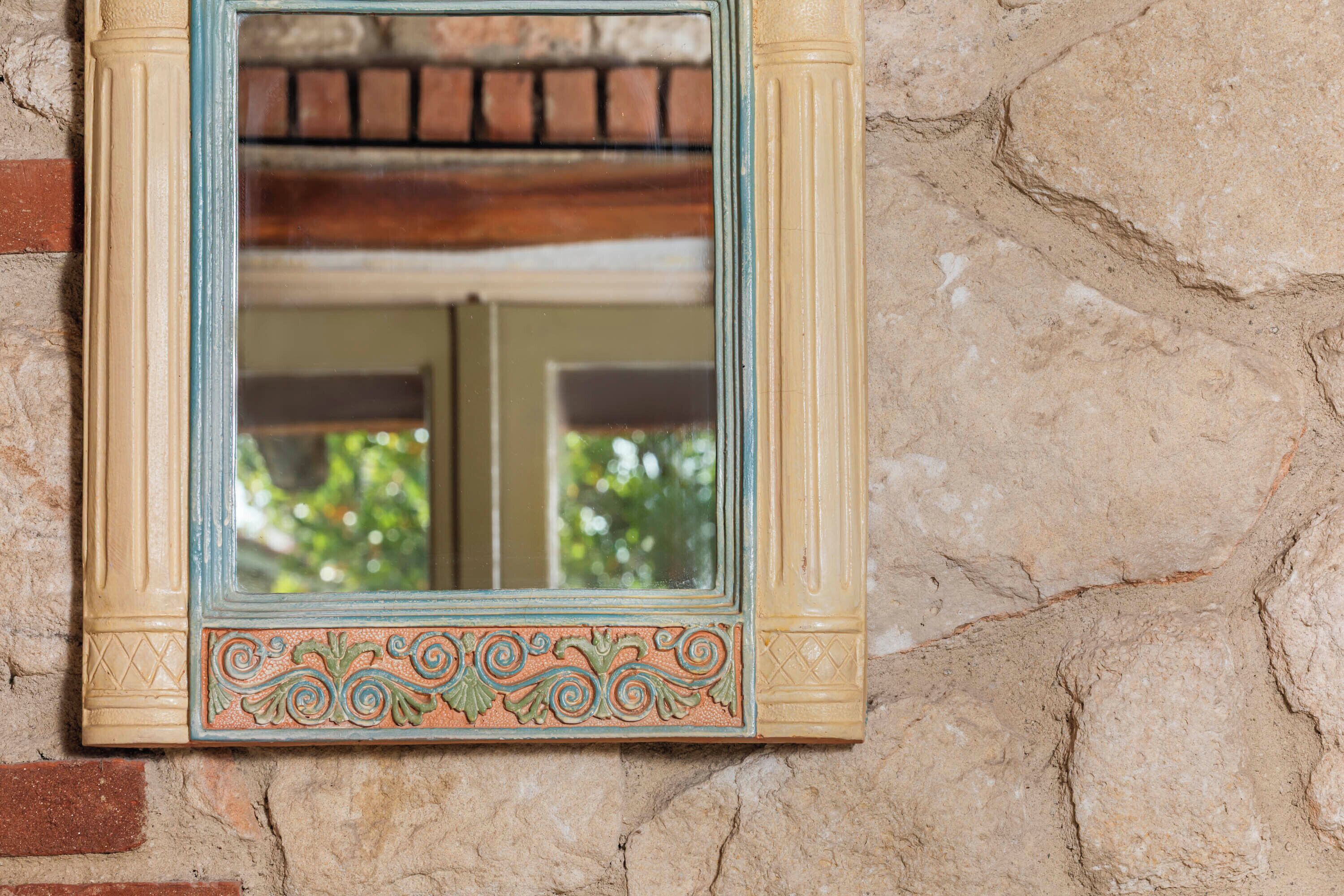 A mirror with ornate frame against a textured stone wall.