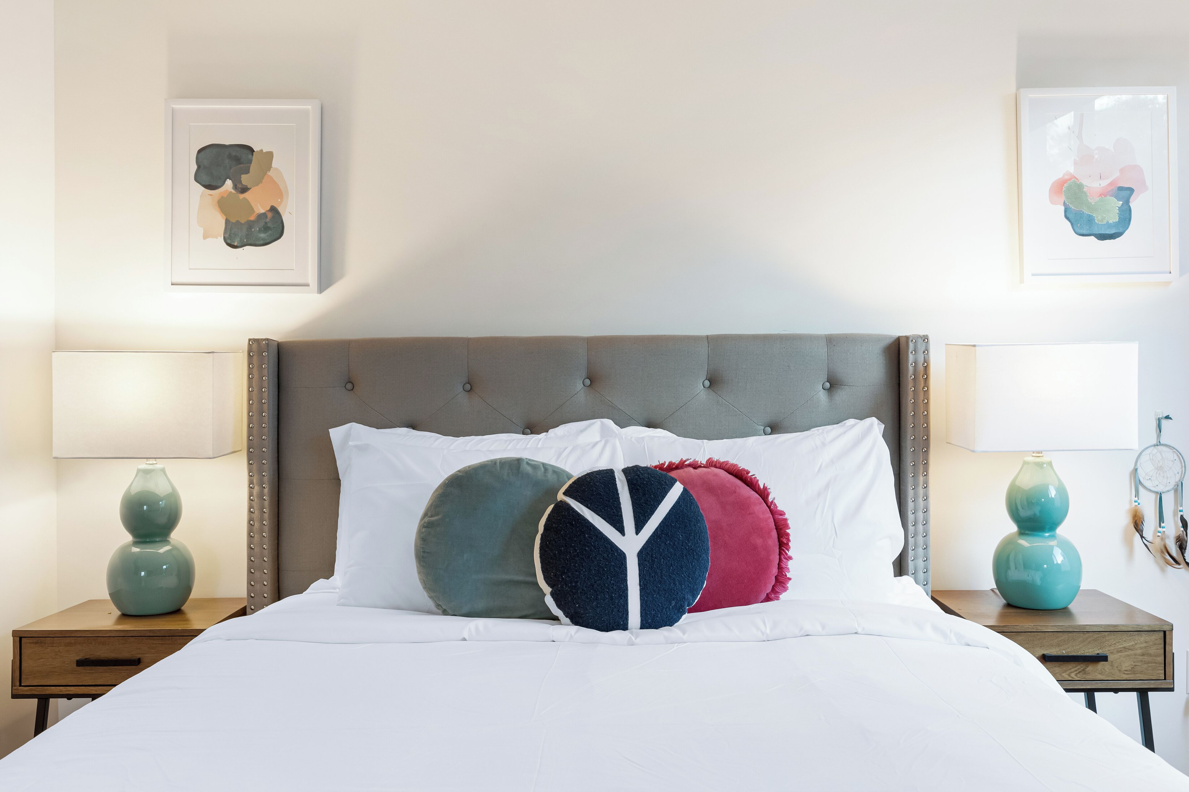 A neatly made bed with a tufted headboard, two bedside tables with lamps, and two framed artworks on the walls.