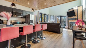 A modern kitchen with a central island, bar stools, and a dining area with a table and chairs. - Smoky Mountain Cabin with Indoor Pool + Hot Tub + Views | Dolly's Dreamhouse (Sevierville)