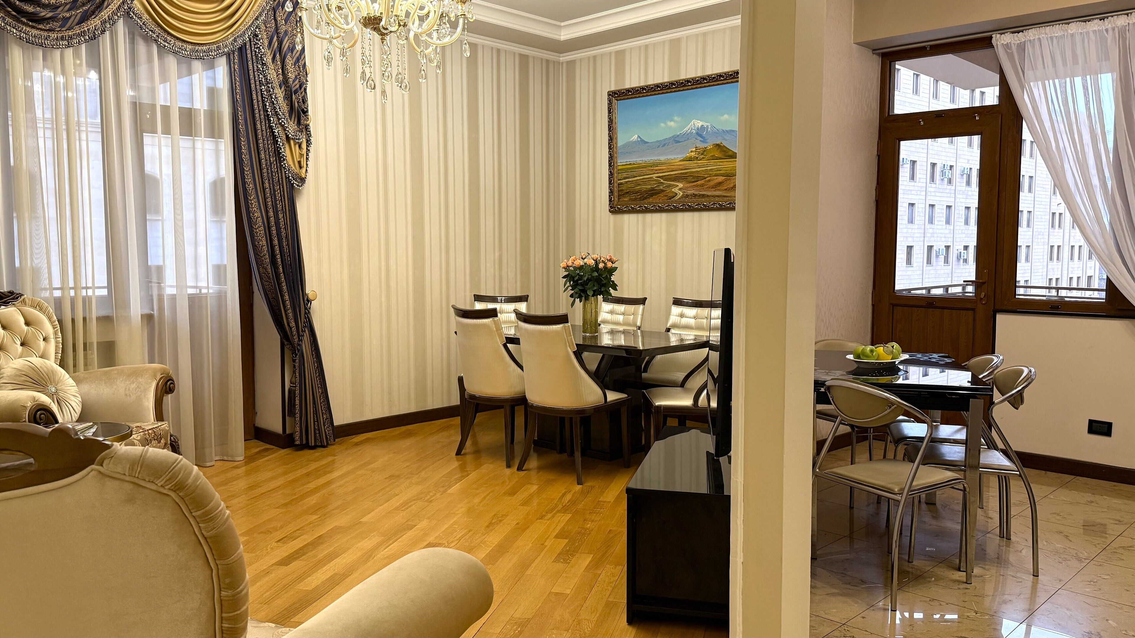 A dining area with a table and chairs, a chandelier, and a painting on the wall.