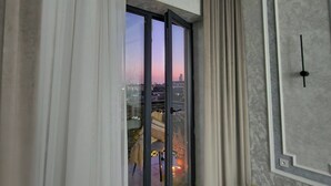 Une pièce spacieuse dotée d’une grande porte-fenêtre coulissante donnant sur un balcon, de rideaux blancs, d’un tapis à motifs et d’un design de plafond moderne.