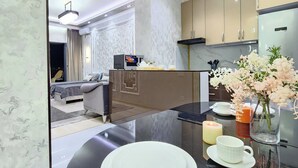 Une cuisine moderne avec un plan de travail en marbre, une table à manger dressée avec des assiettes, des tasses et des couverts, et un vase rempli de fleurs.