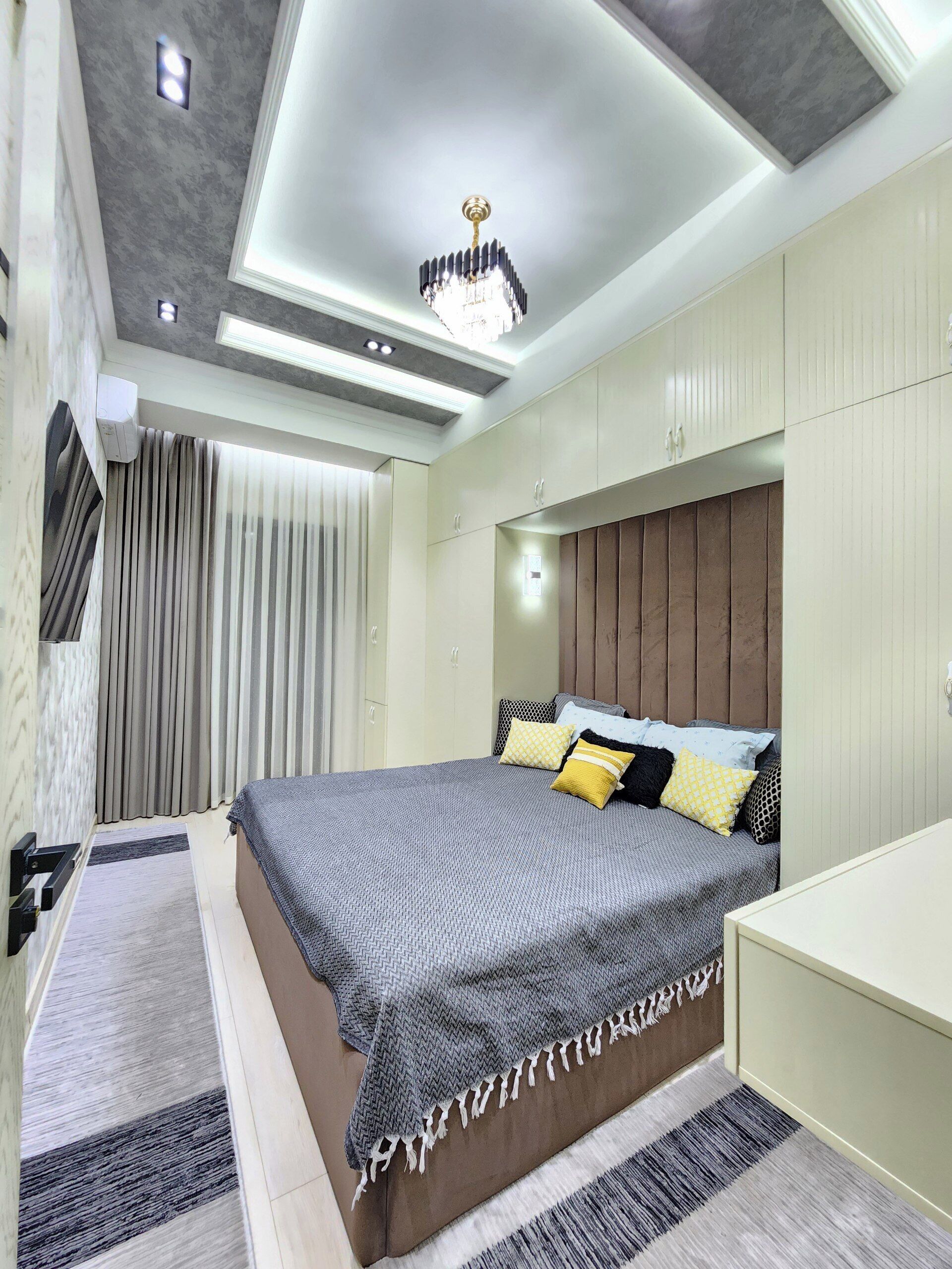 A modern bedroom with a large bed, a built-in wardrobe, and a ceiling light fixture.