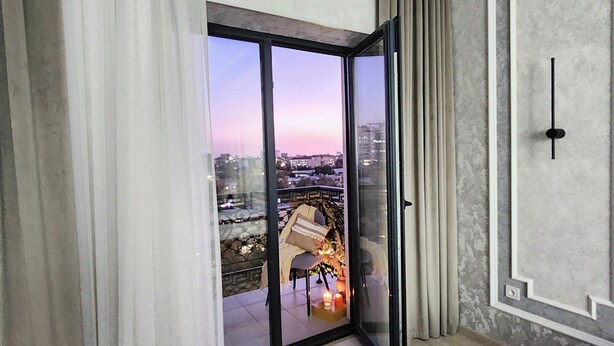Une chambre moderne dotée d’une grande porte-fenêtre coulissante donnant sur un balcon. La chambre est agrémentée d’un tapis à motifs, d’un luminaire fixé au mur et d’un panneau décoratif.