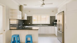 Une cuisine moderne avec des meubles blancs, un plan de travail en granit noir, un réfrigérateur en acier inoxydable et deux tabourets bleus.
