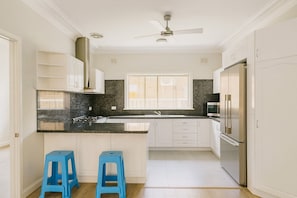 A modern kitchen with white cabinetry, a black granite countertop, a stainless steel refrigerator, and two blue stools. - Modern 4 Bedrooms Home | Free Parking | Walk to Station (Sefton)