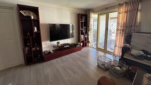 Un salon doté d’un grand téléviseur à écran plat, d’un meuble de rangement en bois et d’une porte-fenêtre coulissante donnant sur un balcon.