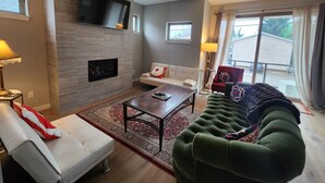 Una sala de estar moderna con chimenea, un televisor de pantalla plana montado en la pared, un sofá blanco y un sofá verde, además de una mesa de centro.