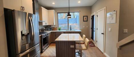 A modern kitchen with stainless steel appliances, a central island, and a view of the outdoors.
