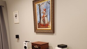 Una habitación con una radio antigua sobre una cómoda, un cuadro enmarcado en la pared y un altavoz en el suelo.