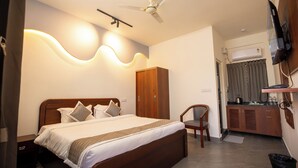 A neatly arranged bedroom with a bed, a wooden wardrobe, a chair, a television, and an air conditioning unit. - Hotel Miracle Meridian  (Bengaluru)