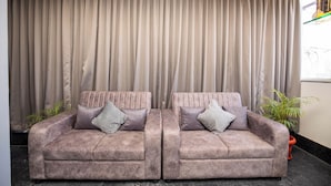 A room with two plush sofas, a large curtain, and a potted plant. - Hotel Miracle Meridian  (Bengaluru)