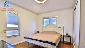A bedroom with a bed, two windows, a bedside table, and a small table with a lamp. - Sea view family relax apartment (Netanya)