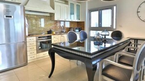 A modern kitchen with a stainless steel refrigerator, a built-in oven, and a glass dining table with chairs. - Sea view family relax apartment (Netanya)